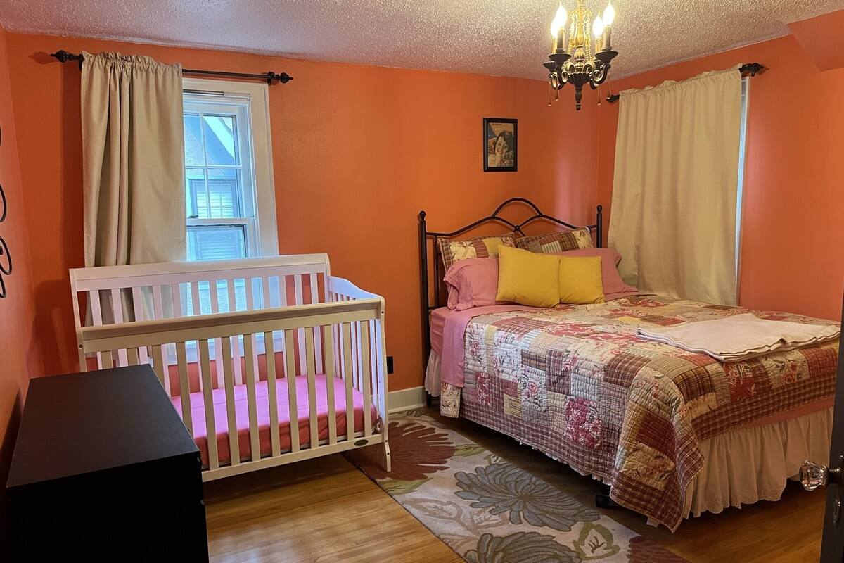 A bedroom with a crib, a bed with a floral quilt, and a chandelier.