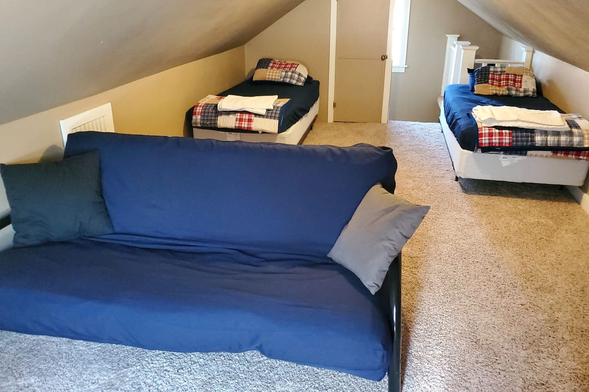 A small, cozy attic bedroom with two beds and a sofa.