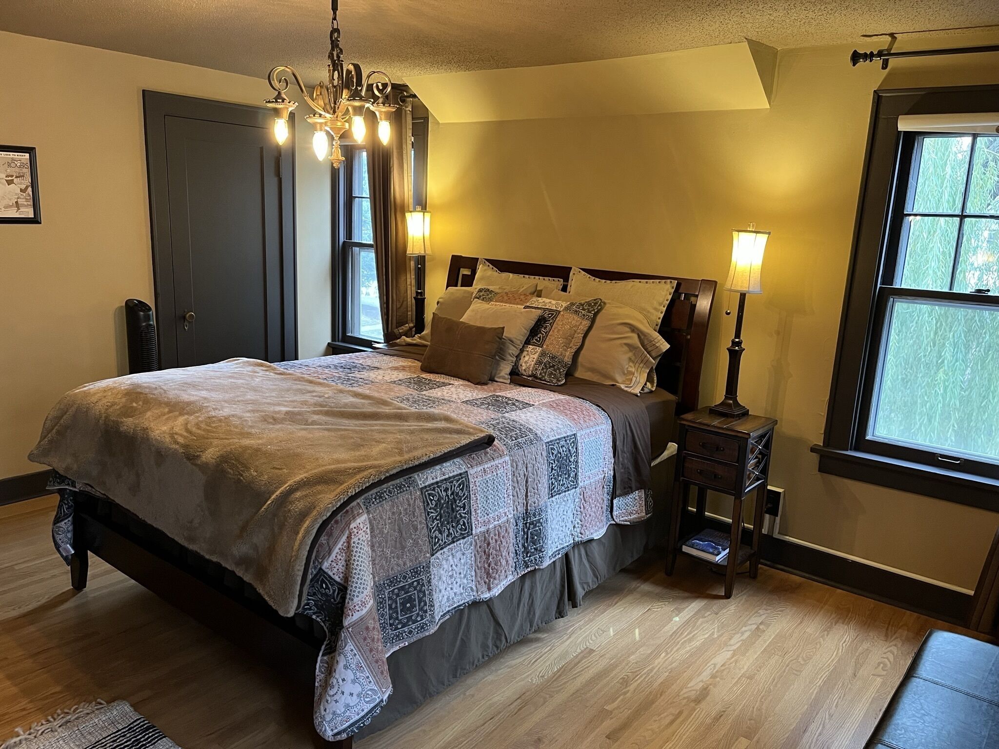 A bedroom with a large bed, a chandelier, a nightstand, and a window with curtains.