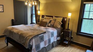 A bedroom with a large bed, a chandelier, a nightstand, and a window with curtains.