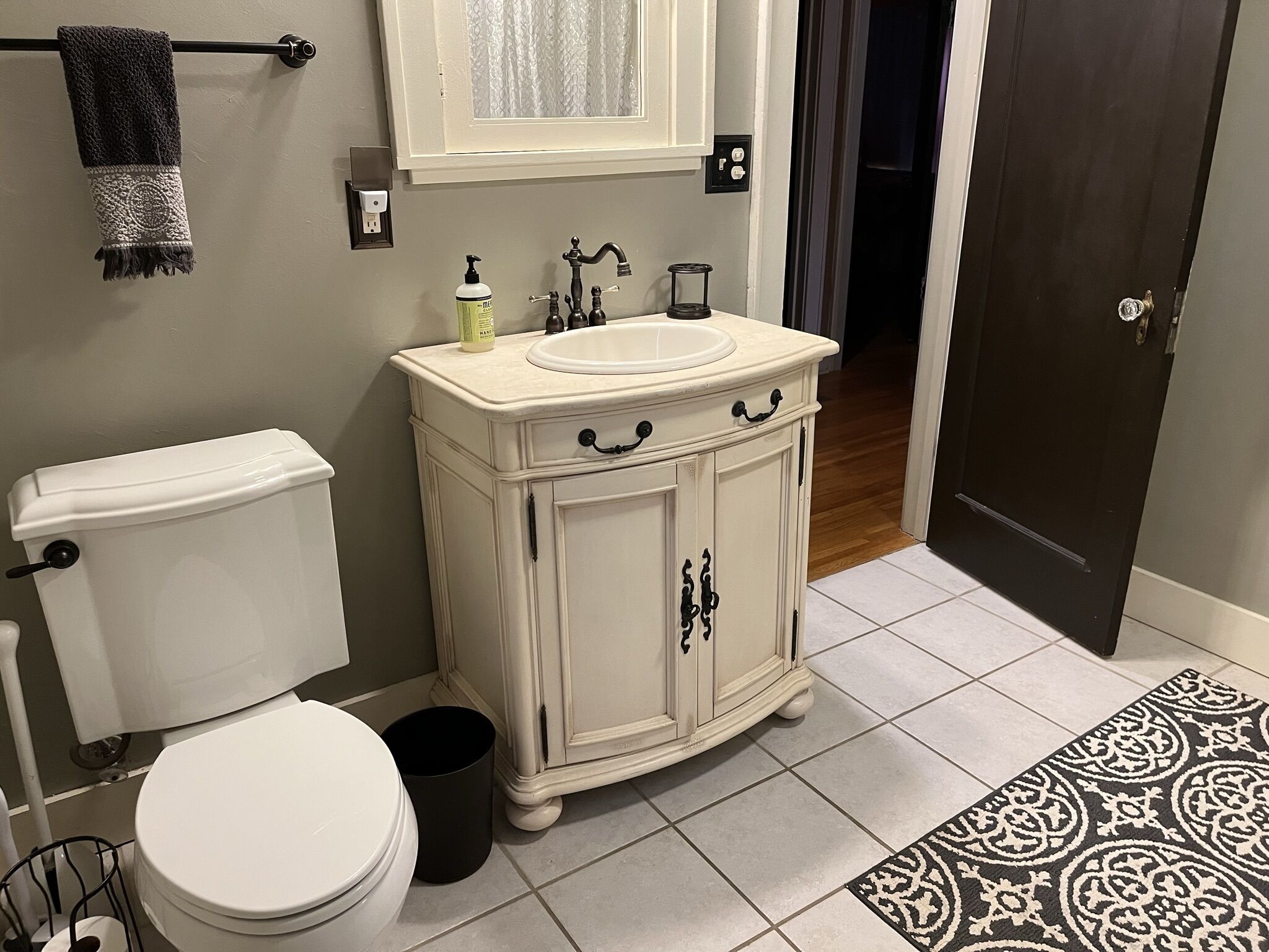 A bathroom with a toilet, sink, cabinet, and a patterned rug.