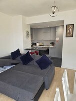 Una sala de estar moderna con un sofá gris, una mesa de comedor y una cocina al fondo.