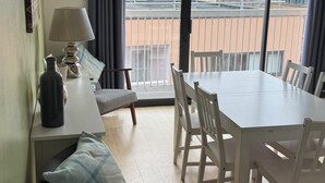 A dining area with a table and chairs, a lamp, a bottle, and a chair with a cushion. - Two Bedroom Balcony Apartment Liverpool  (Liverpool)