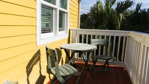 A small outdoor deck with a table and two chairs, a white railing, and a yellow building in the background. - Perfect historic location between beach and strand  (Galveston)