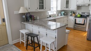 A kitchen with white cabinets, a granite countertop, a sink, a coffee maker, a kettle, and a trash can. - Perfect historic location between beach and strand  (Galveston)