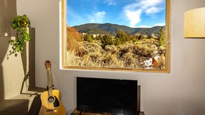 Et værelse med et vindue der ud til et bjergrigt landskab, en guitar og et fladskærms-tv.