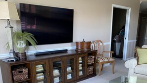 A living room with a flat-screen TV, wicker furniture, a glass coffee table, and a cabinet with storage baskets. - Bright corner unit with Pond View Overlooking Hole 8 at Naples Heritage (Naples)
