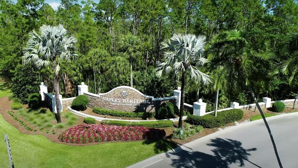 A golf and country club entrance with a stone archway, palm trees, and a landscaped garden. - Bright corner unit with Pond View Overlooking Hole 8 at Naples Heritage (Naples)
