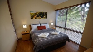 A bedroom with a bed, two bedside tables, a nightstand, a window with blinds, and a painting on the wall.