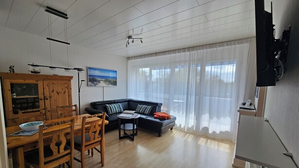 Ein großzügiger Wohnbereich mit einem Holzespeisetisch und Stühlen, einer schwarzen Ledersofa und einem großen Fenster mit transparenten Vorhängen.
