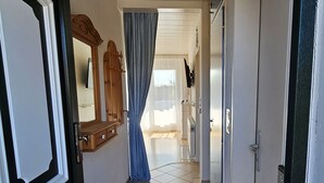 Ein Flur mit Fliesenboden, einer Tür mit schwarzem Rahmen, einem Holzschrank und einem blauen Vorhang.