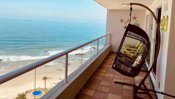Un balcón con una silla colgante que da a una playa con piscina.