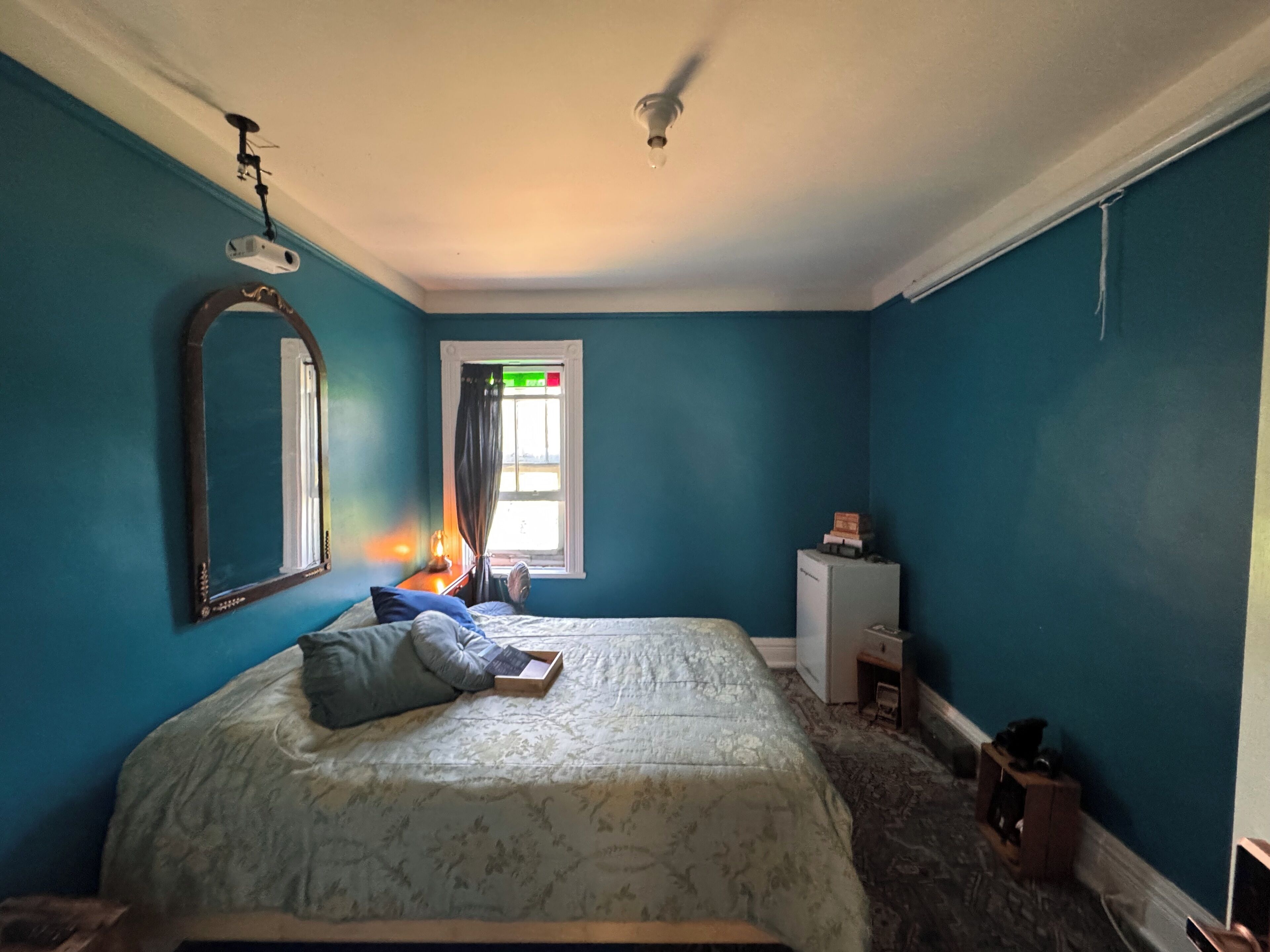 Een slaapkamer met een bed, een spiegel, een raam en een plafondventilator.