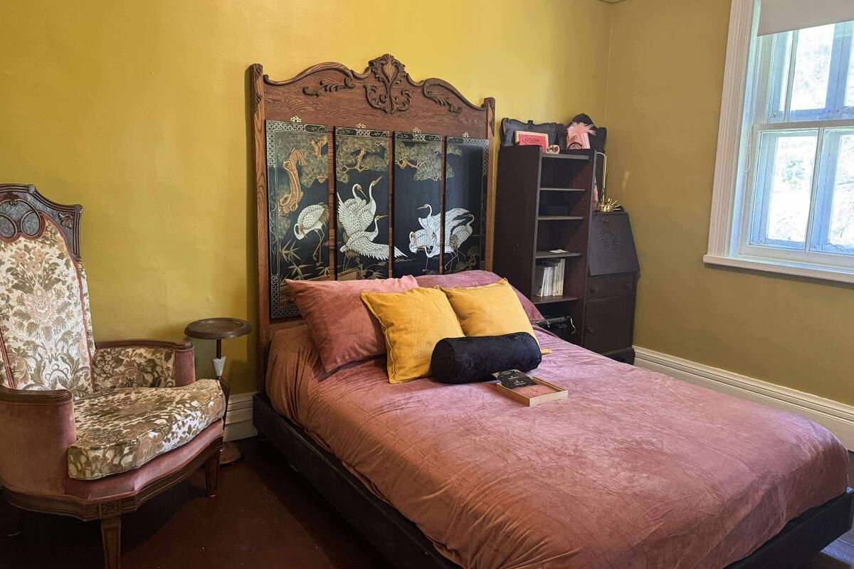 A bedroom with a large bed, a wooden headboard, a chair, and a bookshelf.