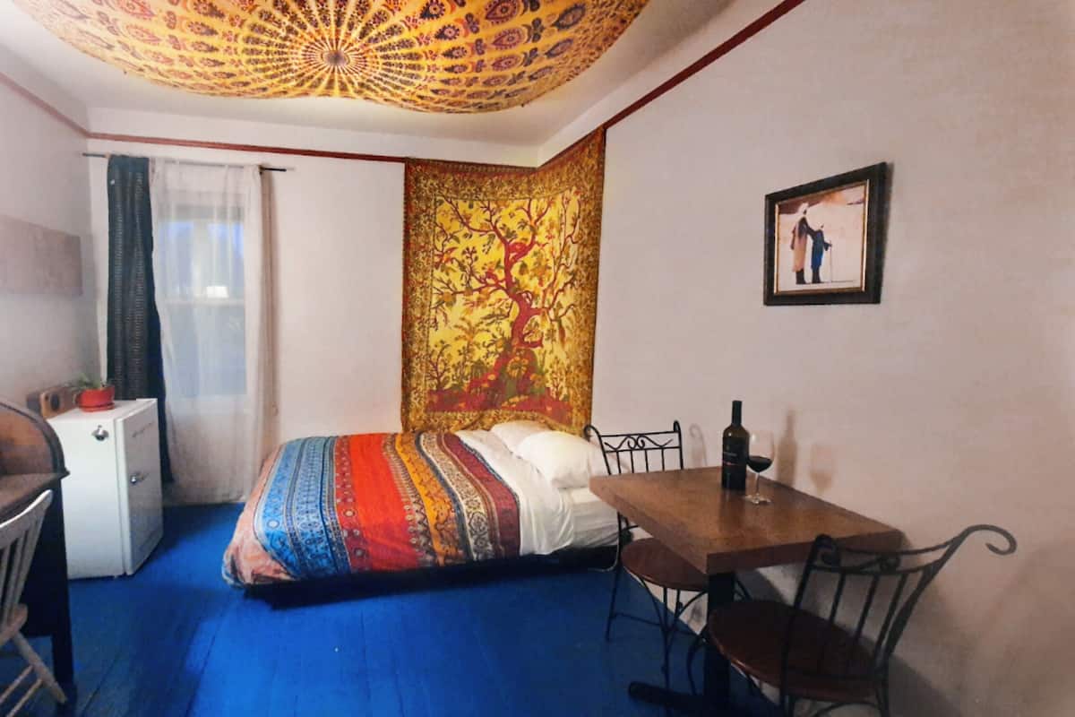A room with a bed, a desk, a chair, a table, and a tapestry on the wall.