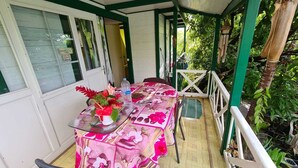 A covered outdoor dining area with a table set for two, surrounded by greenery. - Gite Creole (VIEUX-HABITANTS)