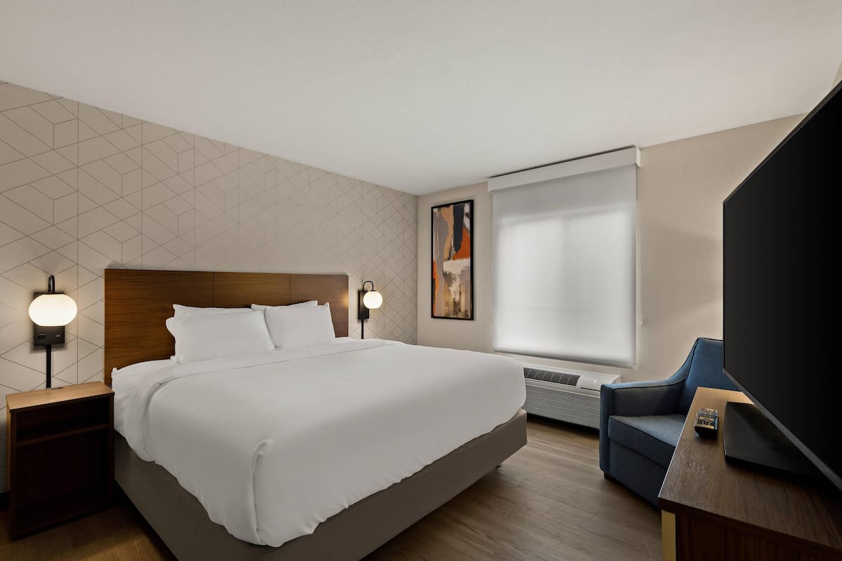 A hotel room with a large bed, a flat-screen TV, a sofa, and a wall-mounted heater.