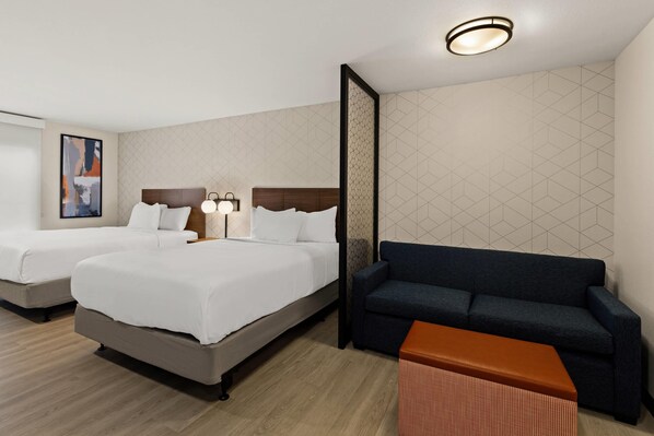 A hotel room with two beds, a sofa, a small table, and a wall with geometric patterns.