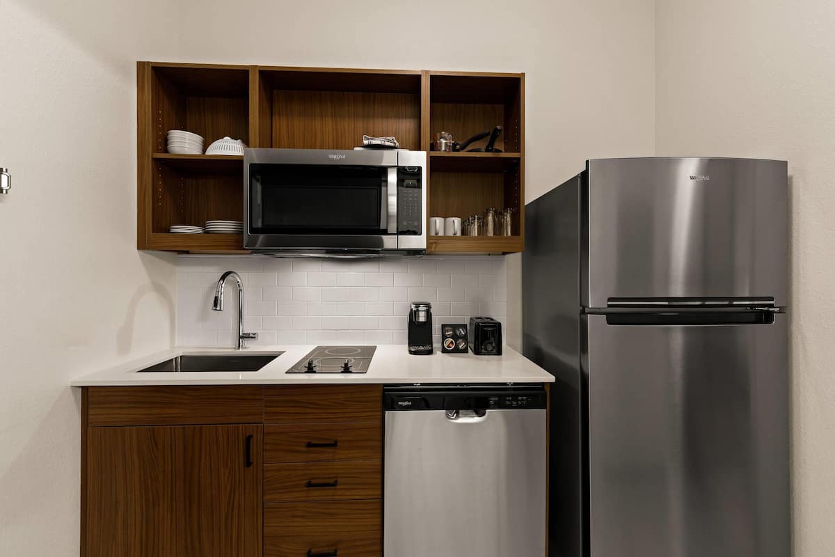 A compact kitchen with a built-in microwave, a stainless steel refrigerator, wooden cabinets, and a dishwasher.