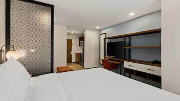 Een moderne hotelkamer met een groot bed, een bureau met een televisie en een kitchenette op de achtergrond.