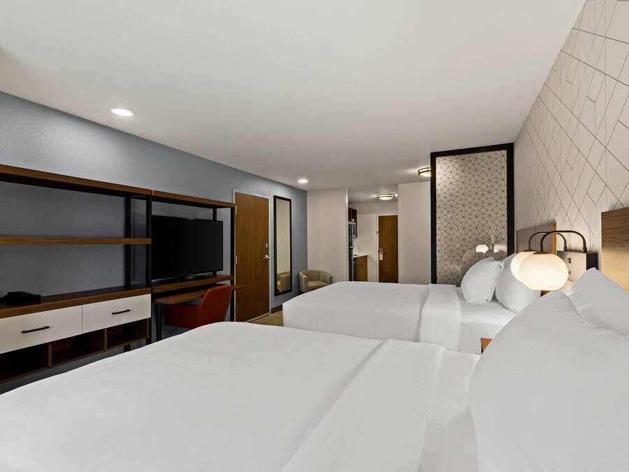 Habitación de hotel con dos camas, un escritorio con televisor y una zona de estar con una silla.