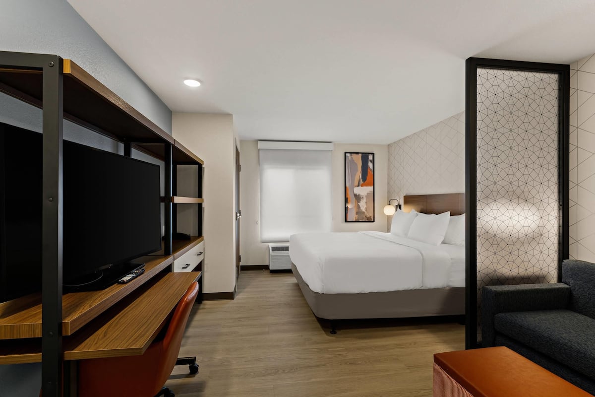 A hotel room with a bed, a TV, a desk, and a seating area.