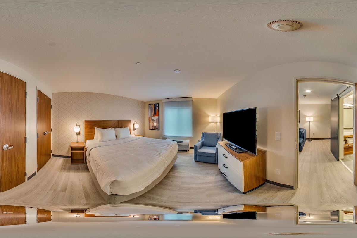 A modern hotel room with a large bed, a TV, a desk, and a mirror.