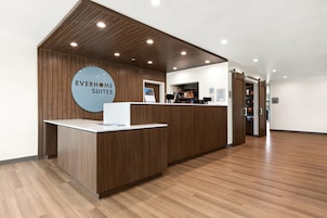 Una recepción con un cartel que dice 'EVERHOMES SUITES' en un moderno vestíbulo de hotel con paneles de madera y suelo de madera.