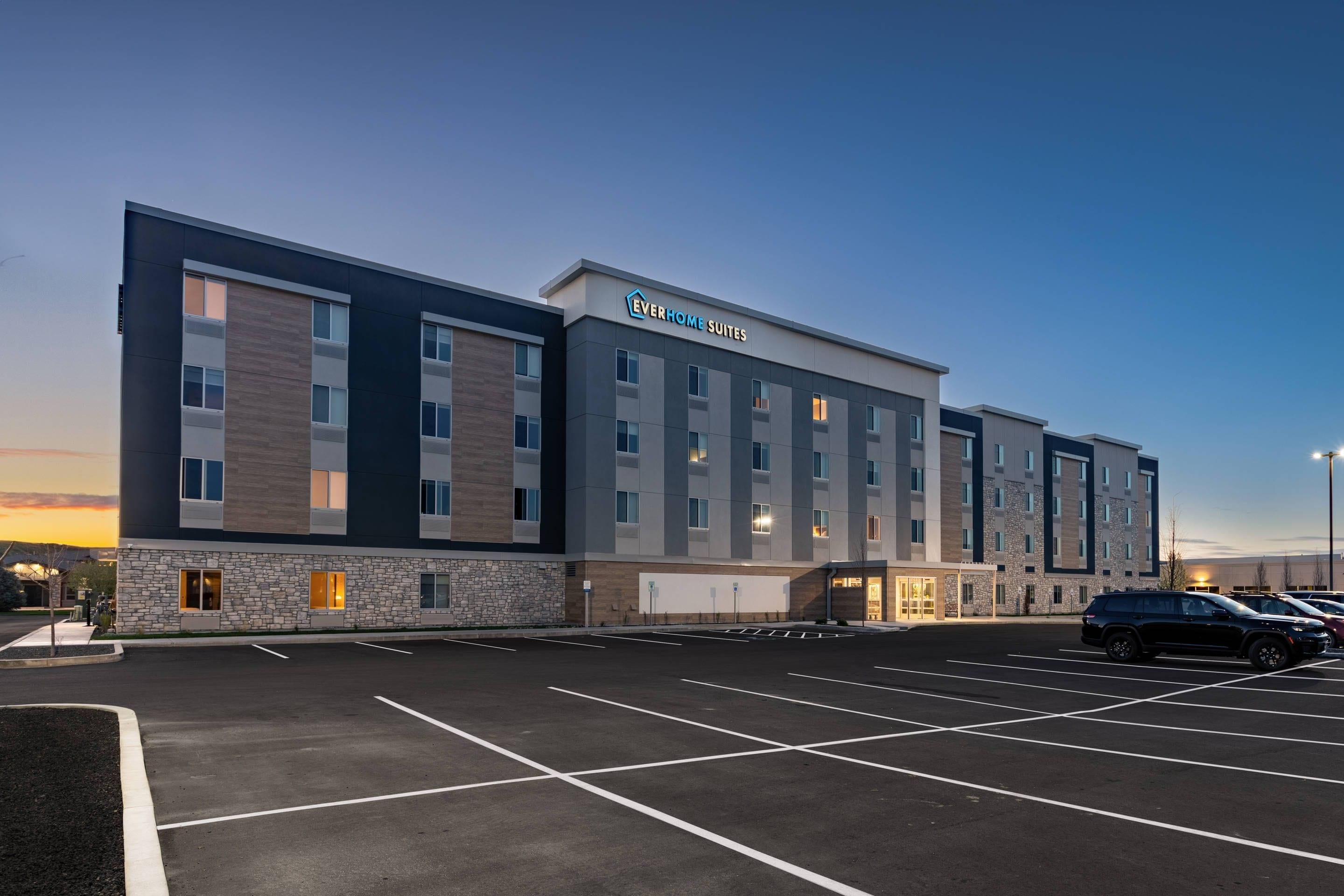 A modern hotel building with a flat roof, multiple windows, and a parking lot.