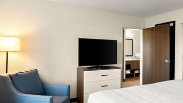 Een hotelkamer met een bed, een tv op een standaard, een bureau met lades, een stoel, een lamp en een zichtbare badkamer door een open deur.