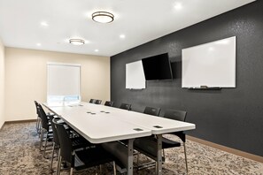 Een vergaderruimte met een lange tafel, stoelen, een whiteboard, een flatscreen-tv en een raam.