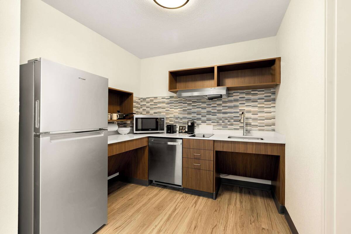A compact kitchen with a refrigerator, microwave, dishwasher, wooden cabinets, and a tiled backsplash.