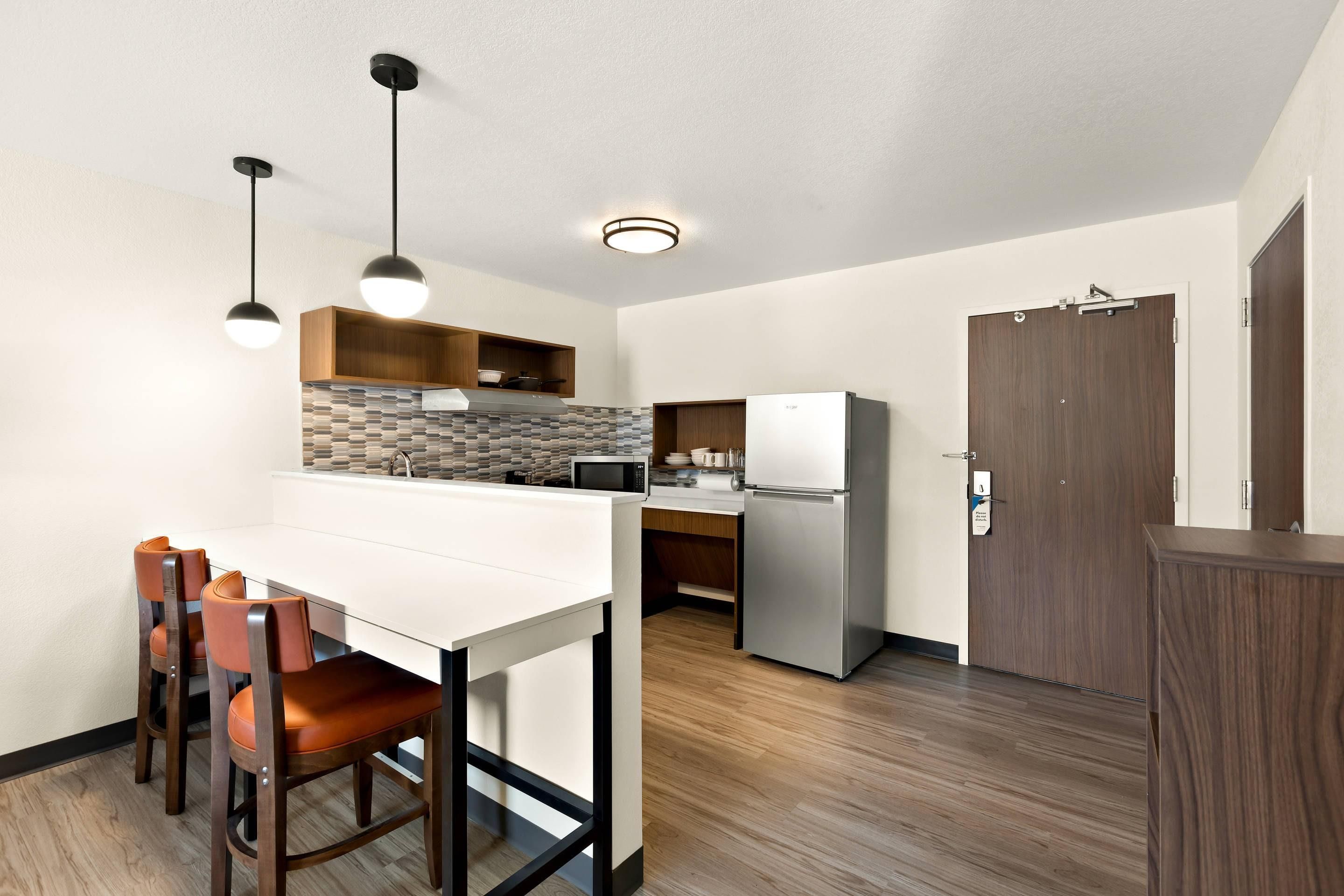 A compact kitchen with a white countertop, two pendant lights, a microwave, and a refrigerator.