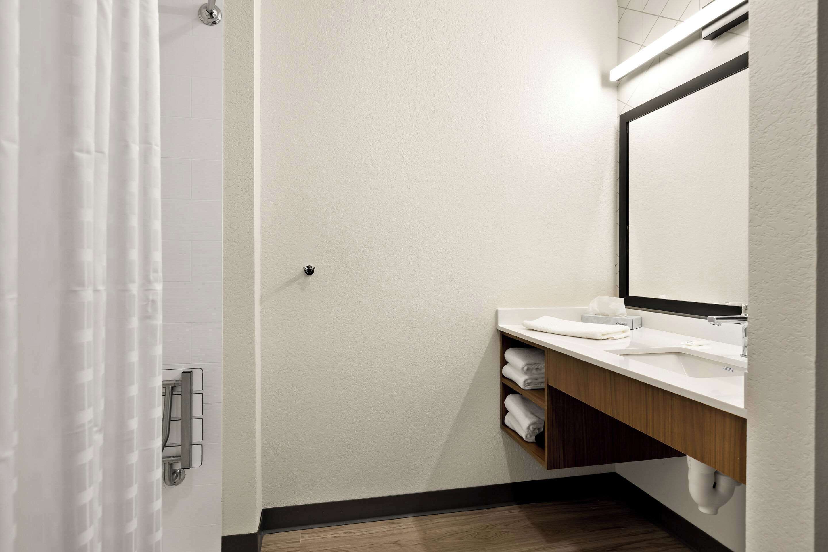 A modern bathroom with a white sink, a mirror, and a shower curtain.