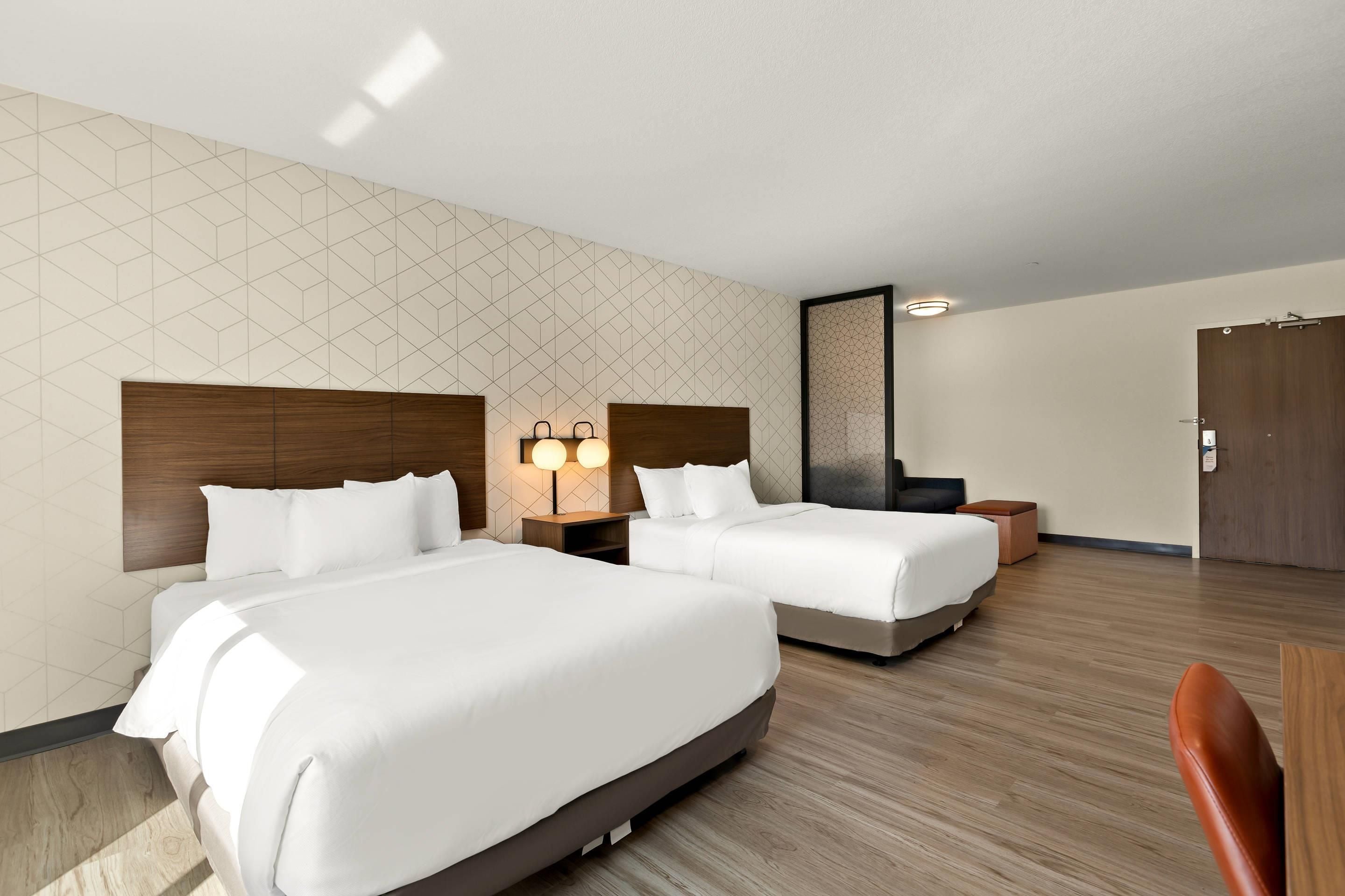 A hotel room with two beds, a wooden headboard, a nightstand with a lamp, and a wooden floor.