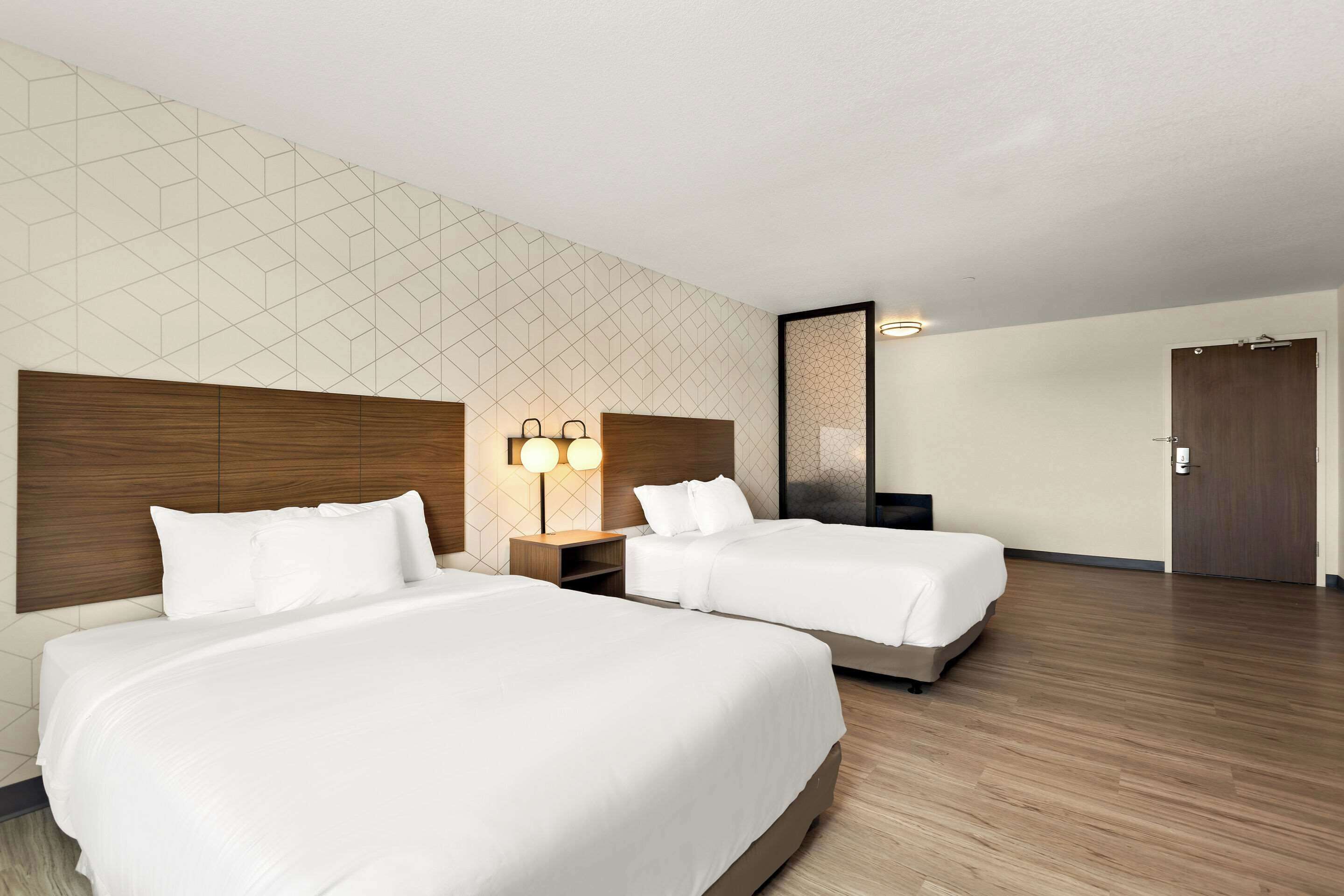 Habitación de hotel con dos camas, cabeceros de madera, pared con diseño geométrico y una puerta.
