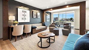 A modern living room with a sofa, two armchairs, a coffee table, and a dining table. There is a large window with a view of the outside. - Everhome Suites Nampa Boise (Nampa)