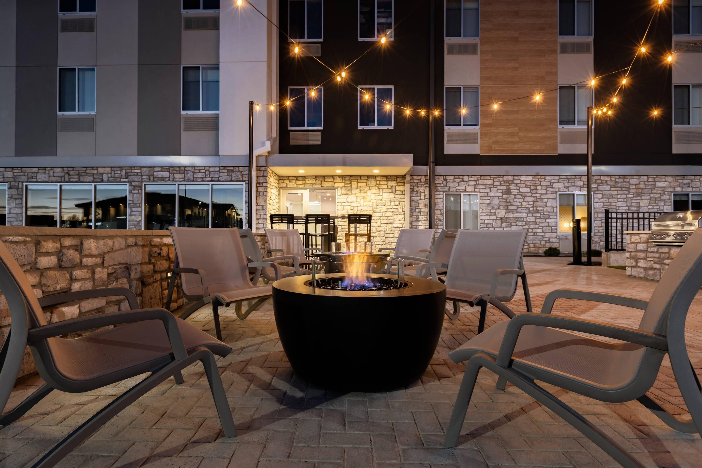 An outdoor seating area with a fire pit, stone walls, and string lights.