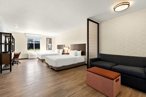 A hotel room with two beds, a desk, a chair, a sofa, and a large window.