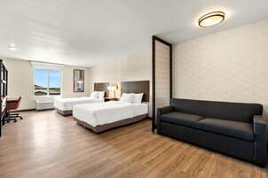 Habitación de hotel con dos camas, un sofá, un escritorio y un ventanal grande.