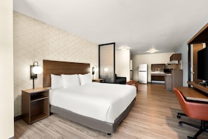A hotel room with a large bed, bedside tables, a desk, a chair, and a kitchenette.