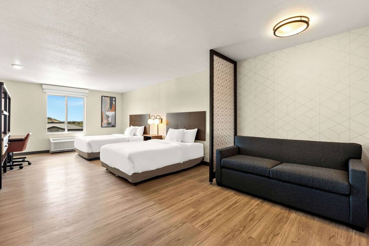 A hotel room with two beds, a sofa, a desk, and a chair.