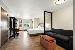 A hotel room with a bed, a desk, a sofa, and a storage ottoman.