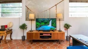 Un salon comprenant un meuble de rangement en bois pour l’équipement audiovisuel, un téléviseur à écran plat, deux lampadaires et un tableau représentant une cascade.