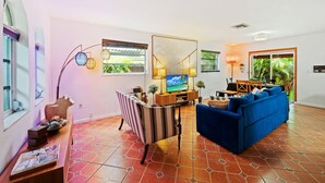 Un salon avec un canapé bleu, un téléviseur, une table à manger avec des chaises et un grand miroir.