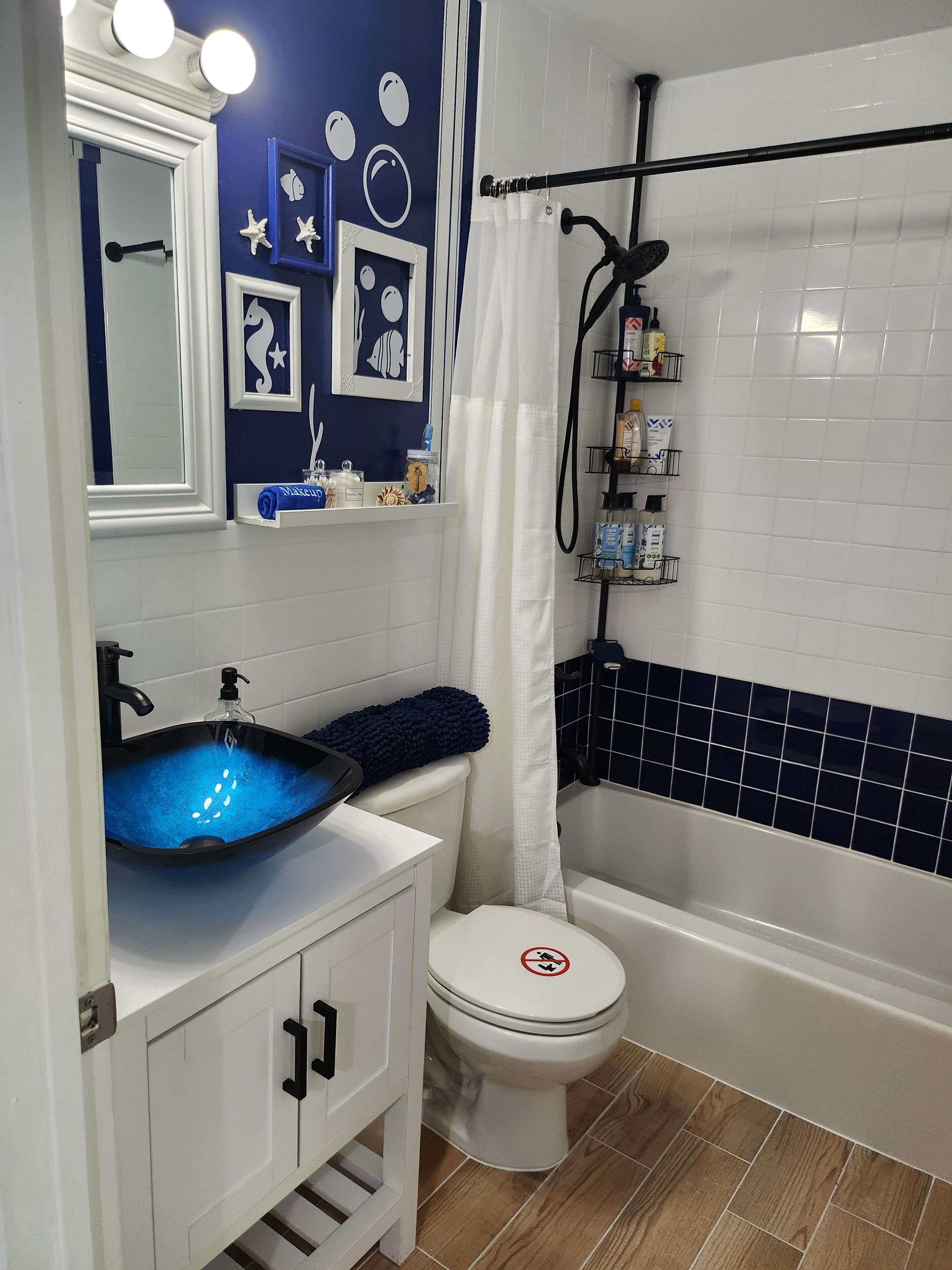 A bathroom with a blue and white color scheme, a white toilet, a blue sink with a glass bowl, and a shower area.