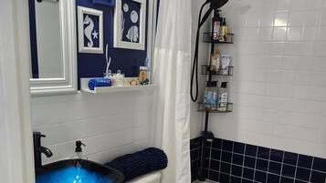 A bathroom with a blue and white color scheme, a white toilet, a blue sink with a glass bowl, and a shower area.
