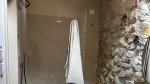 A shower with a glass door, a towel hanging on the wall, and a stone wall.