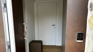 A room with a wooden floor, a white door, and a small ottoman.