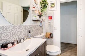 Bathroom features a sink, toilet, shower, and mirror, with patterned tiles and a plant.